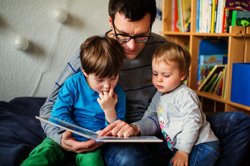 dad reading books with toddler girl and son