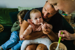 mum feeding baby with dad helping, documentary family photos